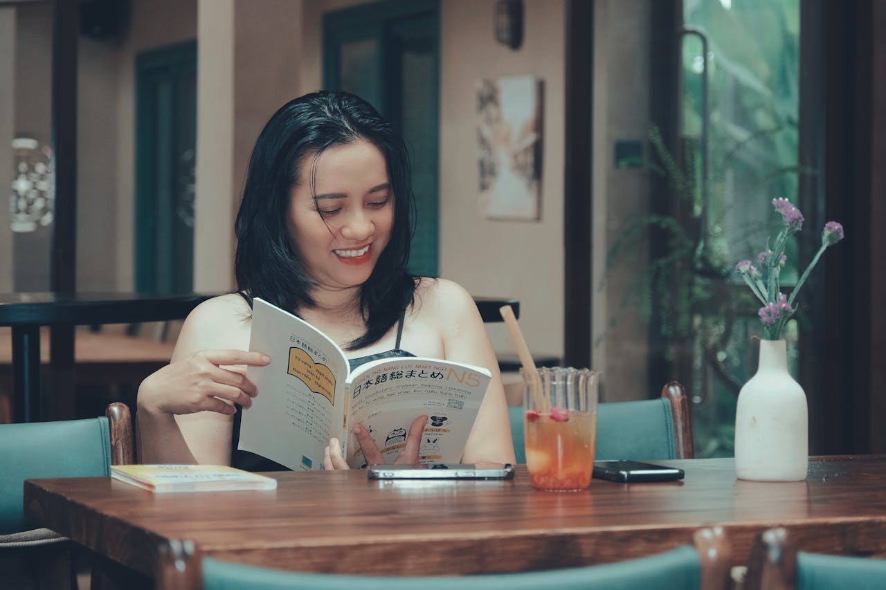 Smiling woman reading a book at a cozy café with a drink nearby.
